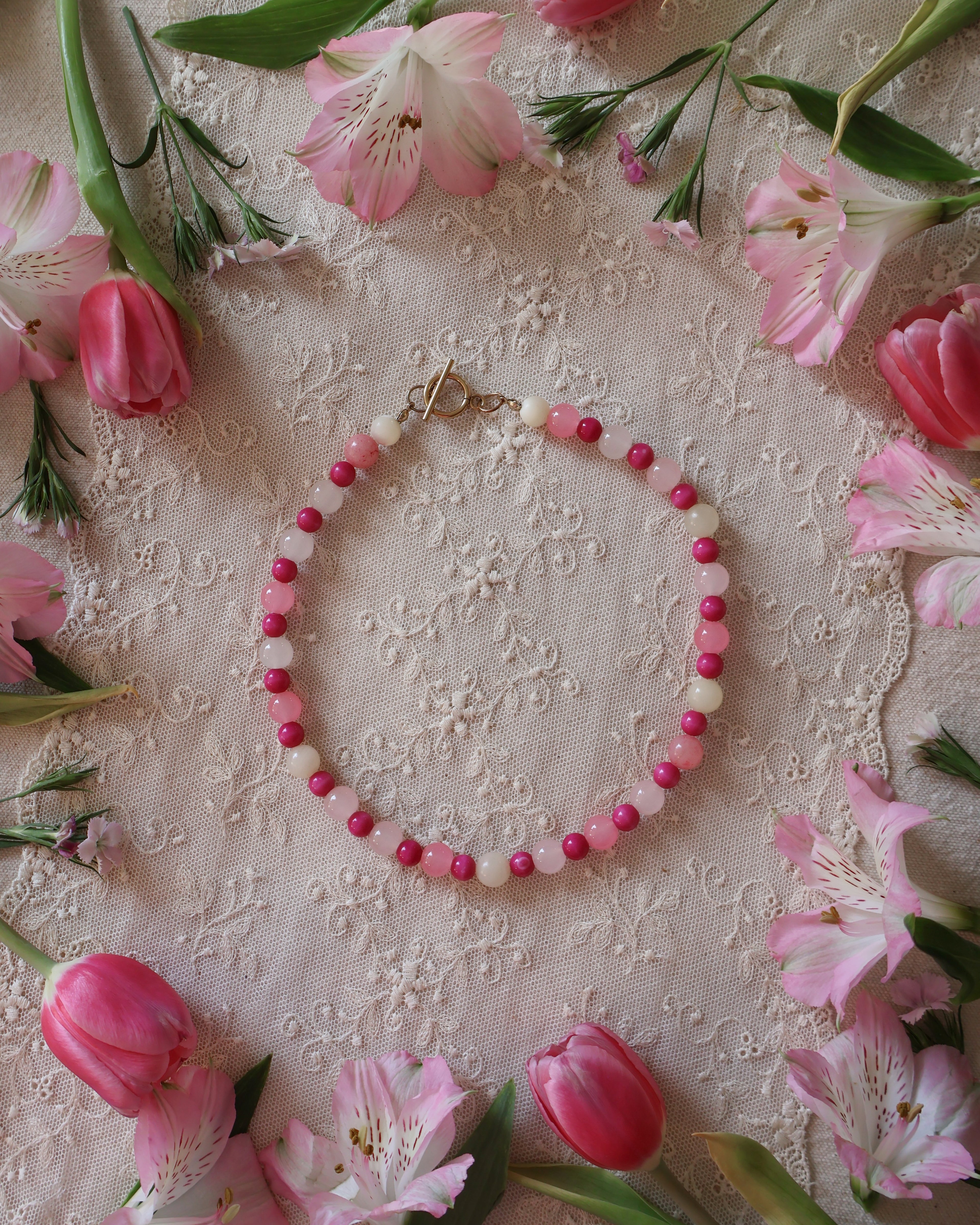 Pink beaded necklace on a decorative fabric background with pink flowers