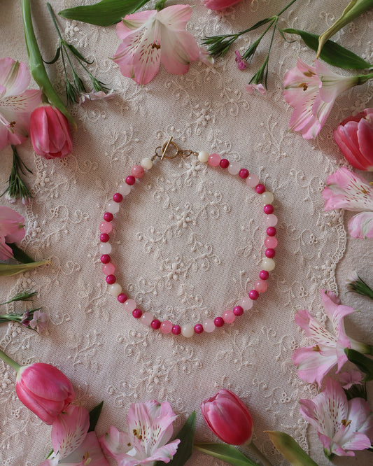 Pink beaded necklace on a decorative fabric background with pink flowers