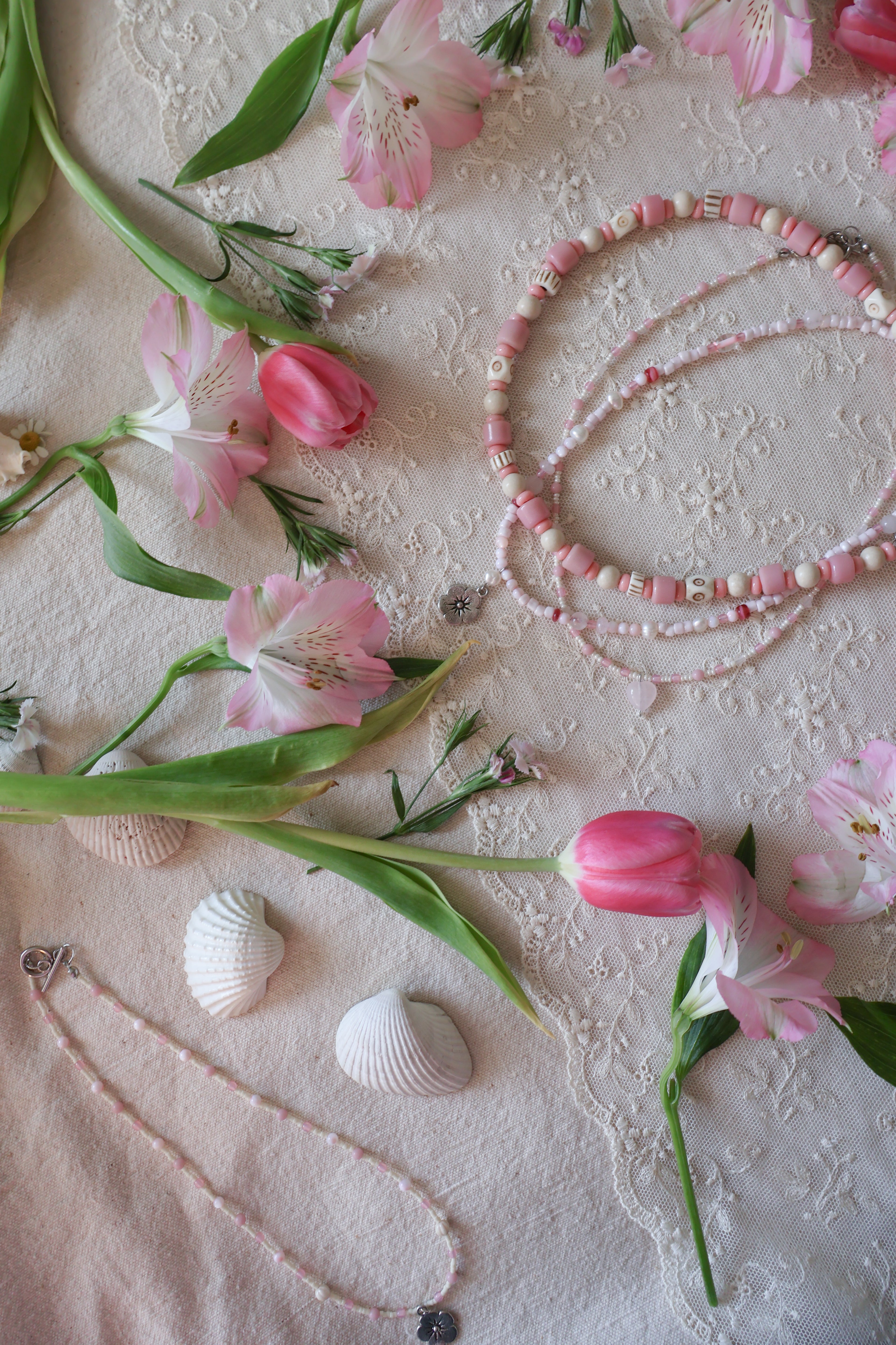Pink beaded necklaces and flowers on a textured surface